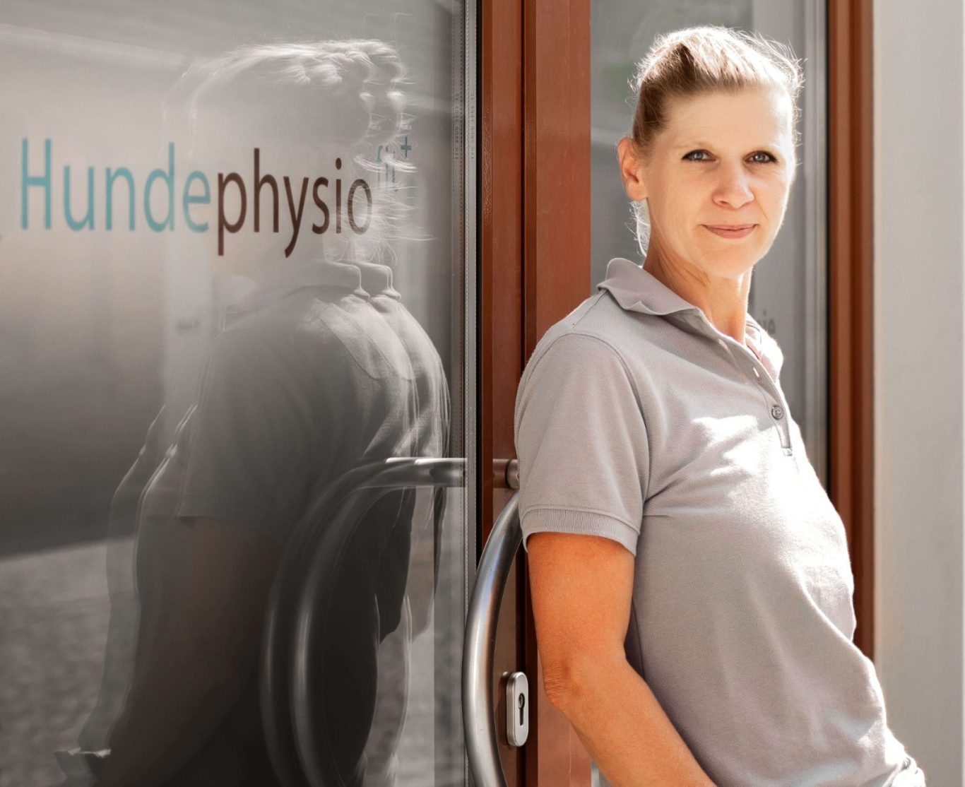 Birgit vor ihrer Praxis in Zossen Frau steht vor einer Praxistür mit dem Schriftzug "Hundephysio".