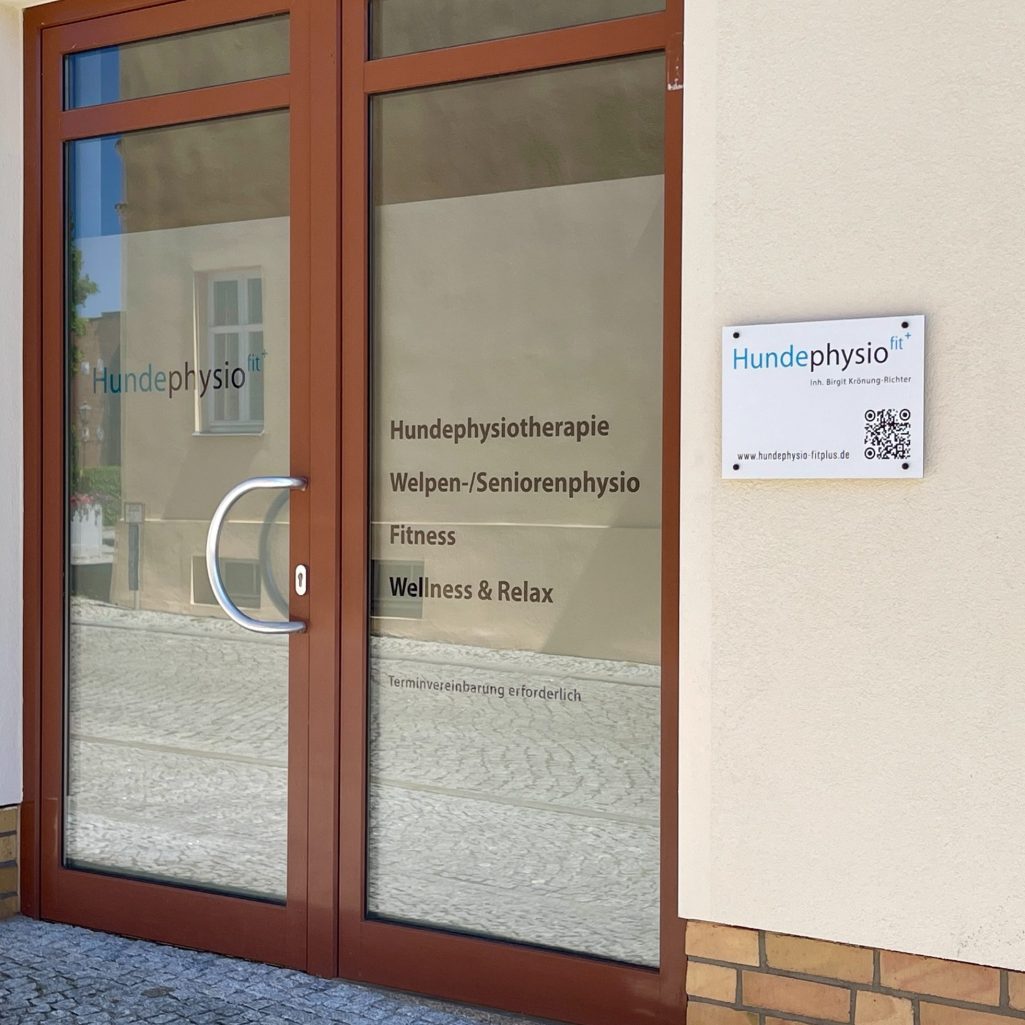 Eingang Hundephysio Fitplus Eingang zu einer Praxis mit Fenstern und einem Schild für die Physiotherapie.