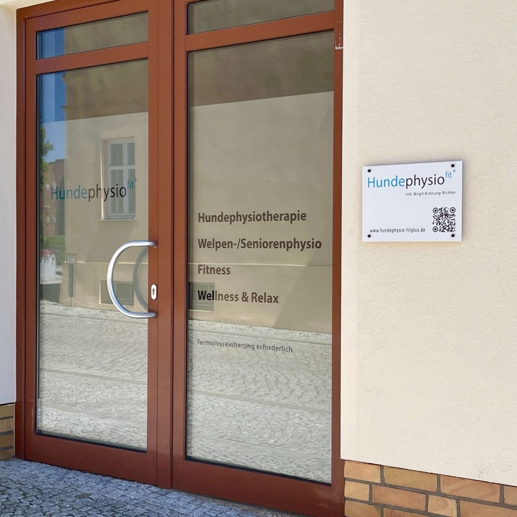 Eingang zur Hundephysio Fitplus-Praxis mit Fenstern und einem Schild für die Physiotherapie.